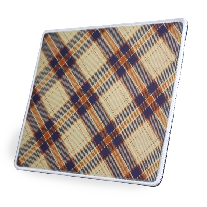 Zijaanzicht - gekanteld naar link - van een stoffen muismat met een witte gestikte rand met een diagonaal ruitpatroon (plaid / tartan) in cremé, marineblauw en oranje kleuren, met kruisende strepen en ruitvormen.